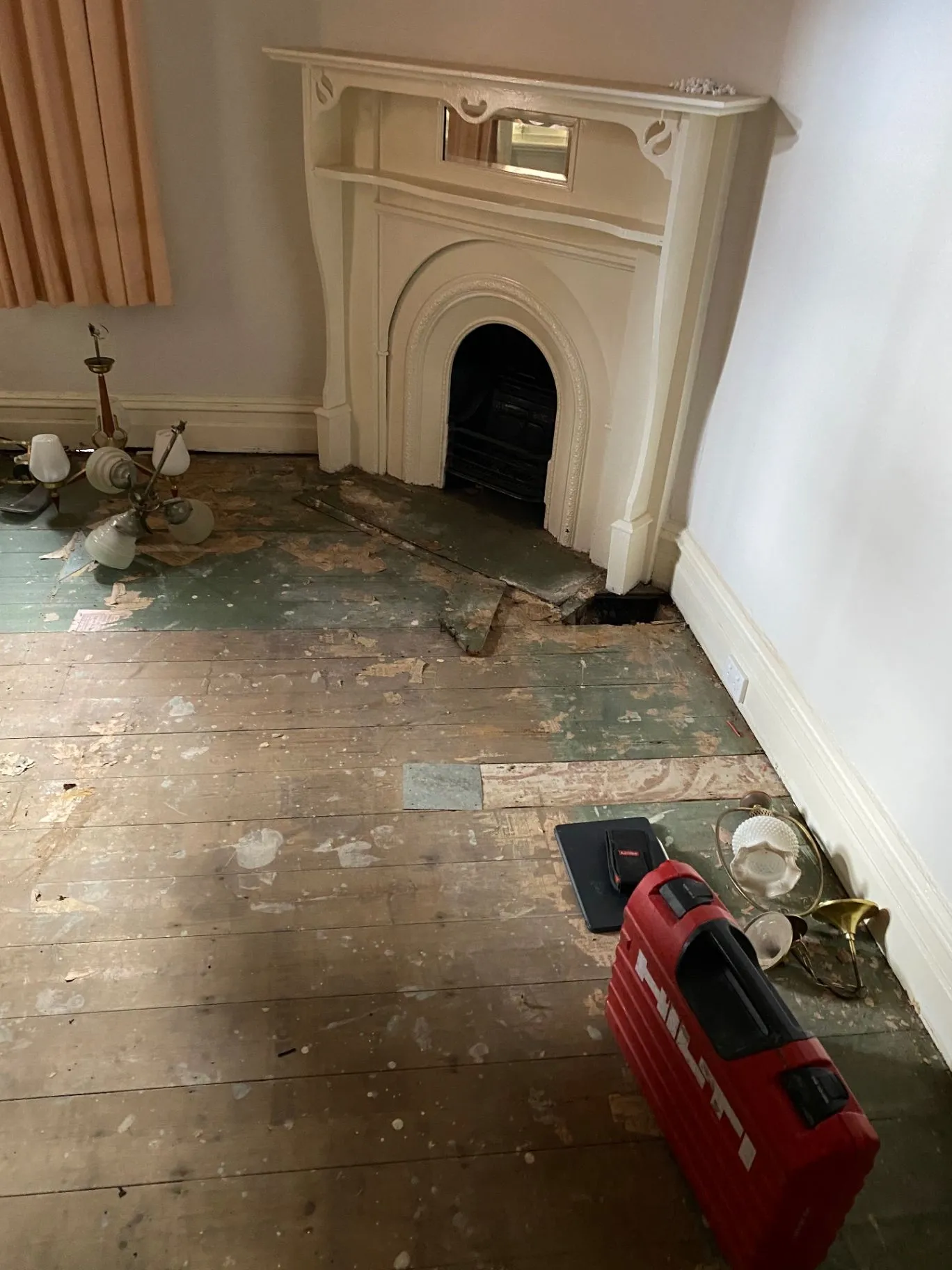 Elsternwick interior with ornate painted fireplace, worn timber floorboards, and repair work underway